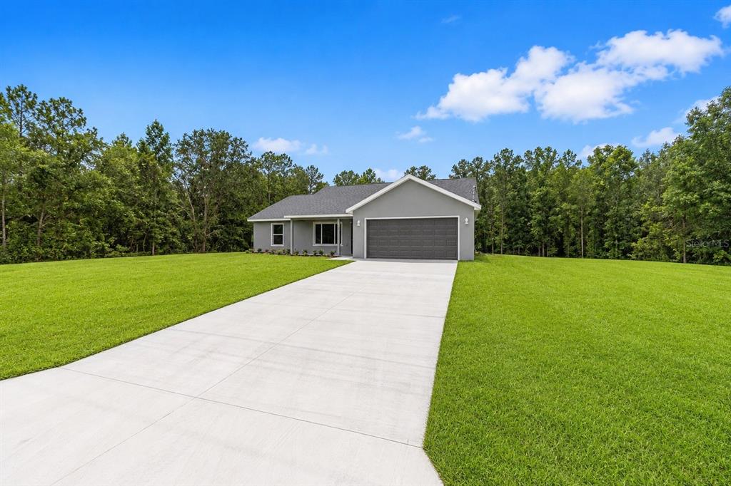 A gray single-story house with a two-car garage sits on a large grassy lot — 22870 SW LIME RIDGE LANE, DUNNELLON, FL