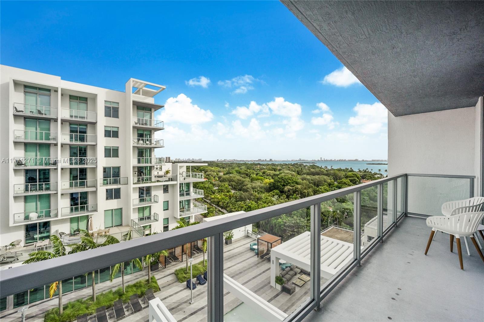 A balcony with white chairs overlooks a modern apartment building, a pool deck, and water — 3900 Biscayne Blvd # 1016, Miami FL 33137, MIAMI, FL