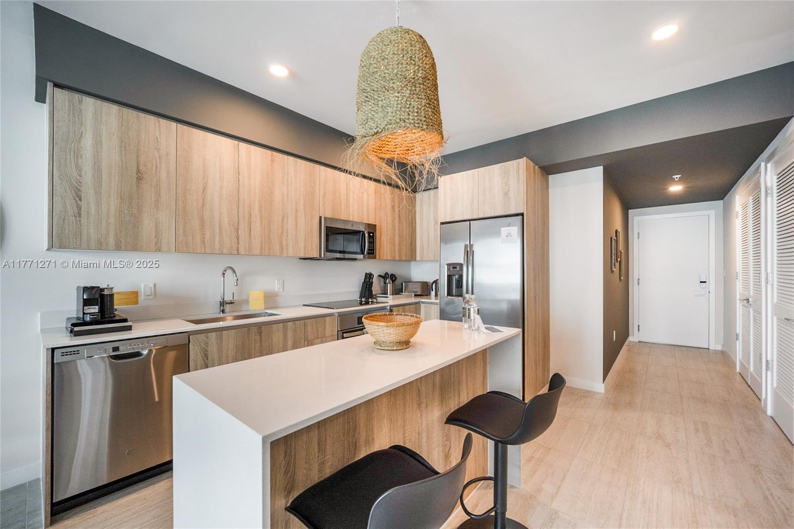 A modern kitchen features light wood cabinetry, white countertops, stainless steel appliances, and two stools — 3900 Biscayne Blvd # 1016, Miami FL 33137, MIAMI, FL