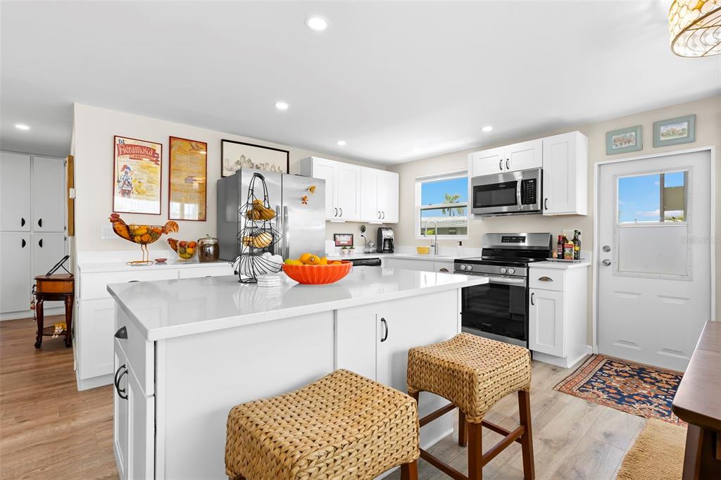 A white kitchen features a central island with woven stools, stainless appliances, and wood flooring — 7165 MOUNT GEORGETOWN DRIVE NE UNIT 571, ST PETERSBURG, FL