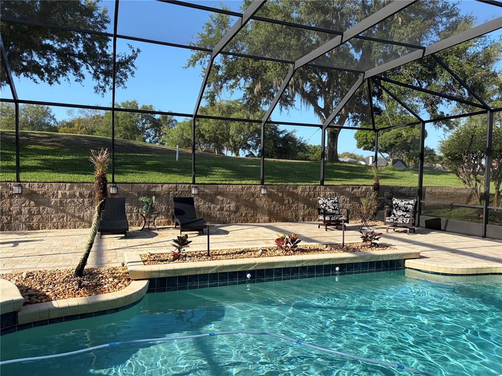 A screened-in pool area features a stone patio, lounge chairs, and a retaining wall — 889 EAGLE CLAW COURT, LAKE MARY, FL