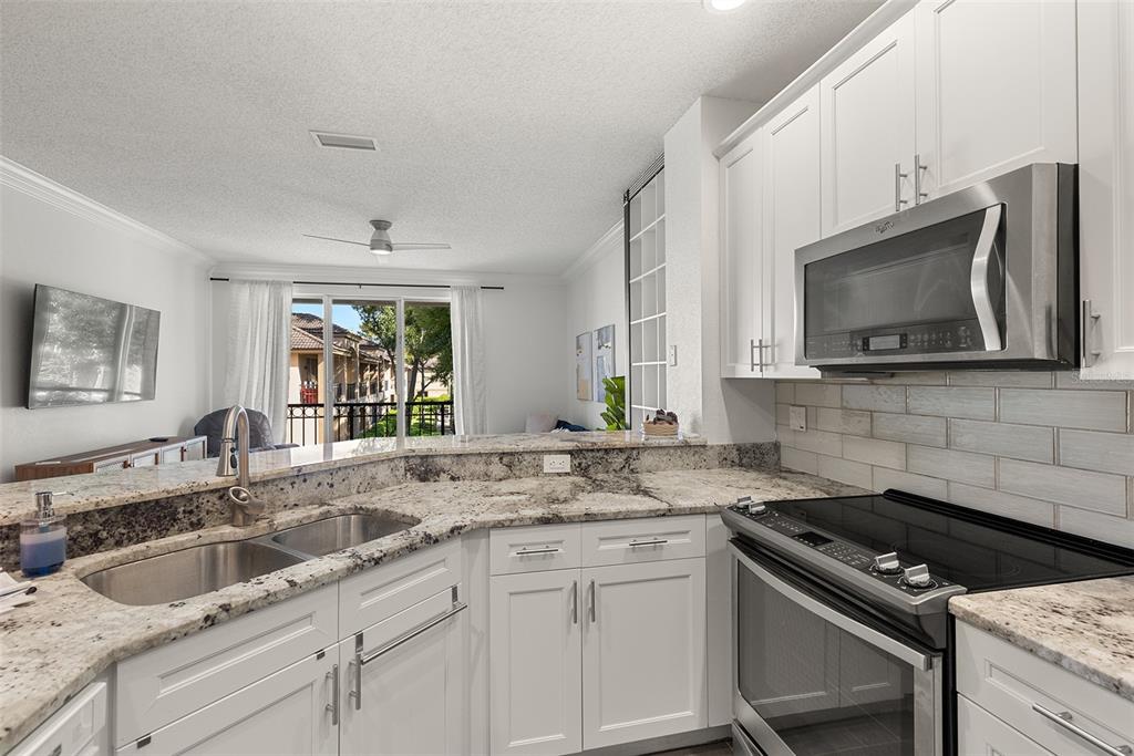 A kitchen with white cabinets, granite countertops, and stainless steel appliances overlooks a living area — 910 NORMANDY TRACE ROAD, TAMPA, FL