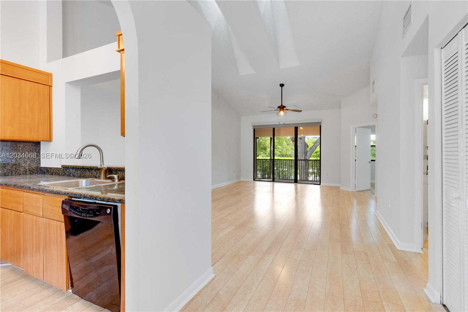 A kitchen with wood cabinets and a dishwasher opens into a bright living area — 104 NW 98th Ter # 104, Plantation FL 33324, PLANTATION, FL