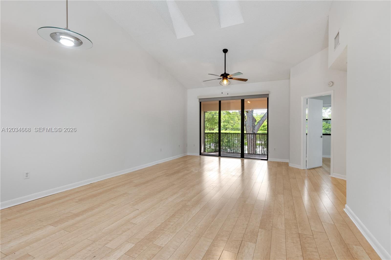 This empty living room features light wood flooring, a vaulted ceiling, and a sliding glass door — 104 NW 98th Ter # 104, Plantation FL 33324, PLANTATION, FL