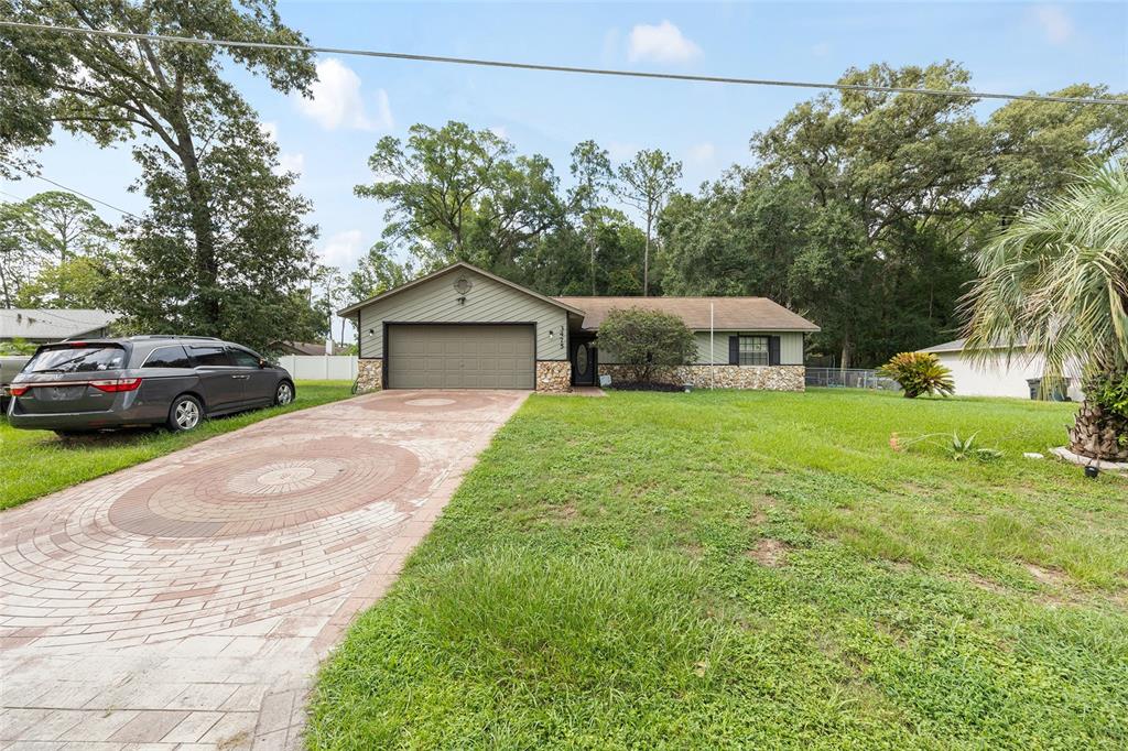 A single-story house with a stone facade, green siding, and a circular patterned brick driveway — 3475 NE 43RD PLACE, OCALA, FL
