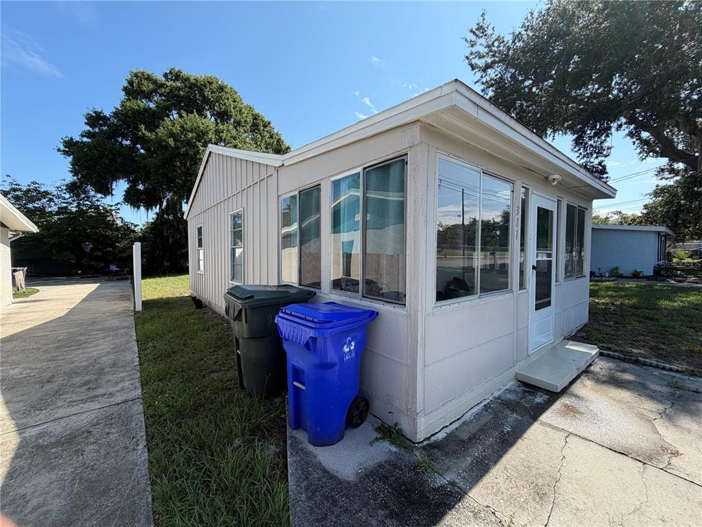 The exterior of a light-colored mobile home features a screened-in porch and two trash bins — 311 W BELLA VISTA STREET, LAKELAND, FL