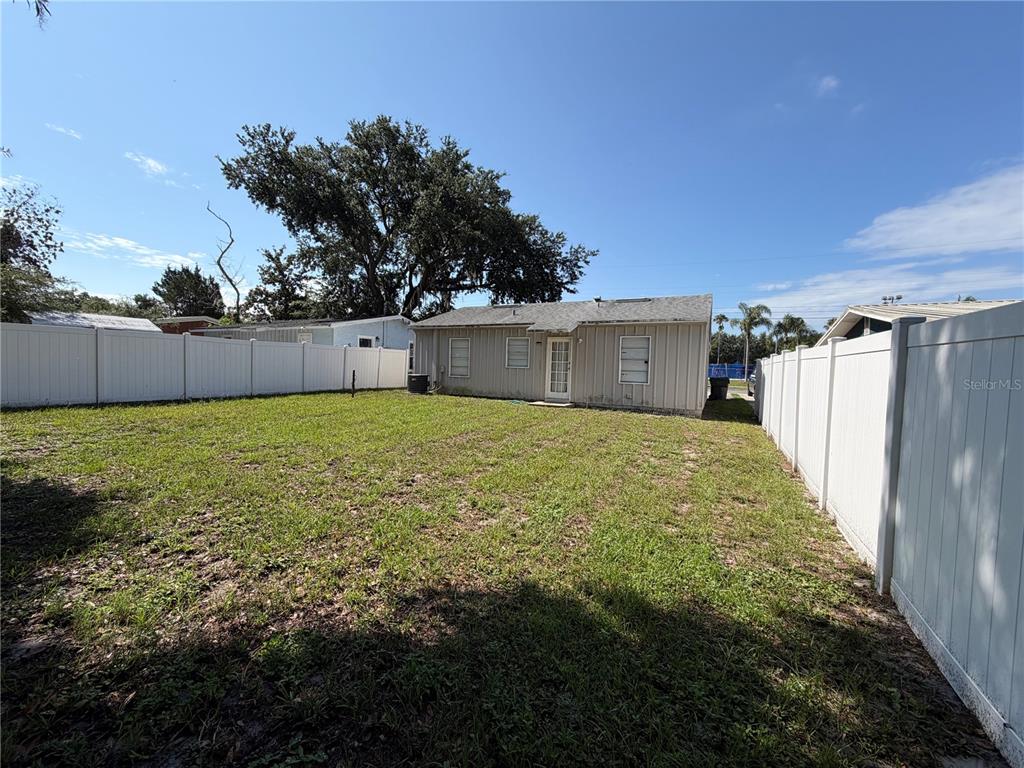 A backyard features a single-story house with light siding, a white fence, and large trees — 311 W BELLA VISTA STREET, LAKELAND, FL