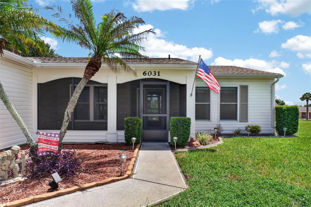 A single-story house features a screened front porch, a concrete walkway, and an American flag — 6031 SANDERLING DRIVE, LAKELAND, FL
