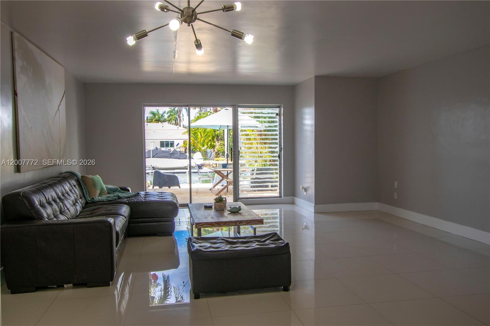 A living room features a dark leather sectional, tile flooring, and sliding doors to a patio — 2117 NE 123rd St, North Miami FL 33181, NORTH MIAMI, FL