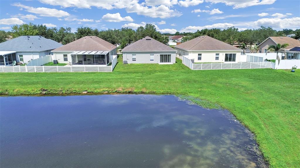 A row of suburban houses with white fences overlooks a pond under a cloudy sky — 11908 FERN BLOSSOM DRIVE, GIBSONTON, FL