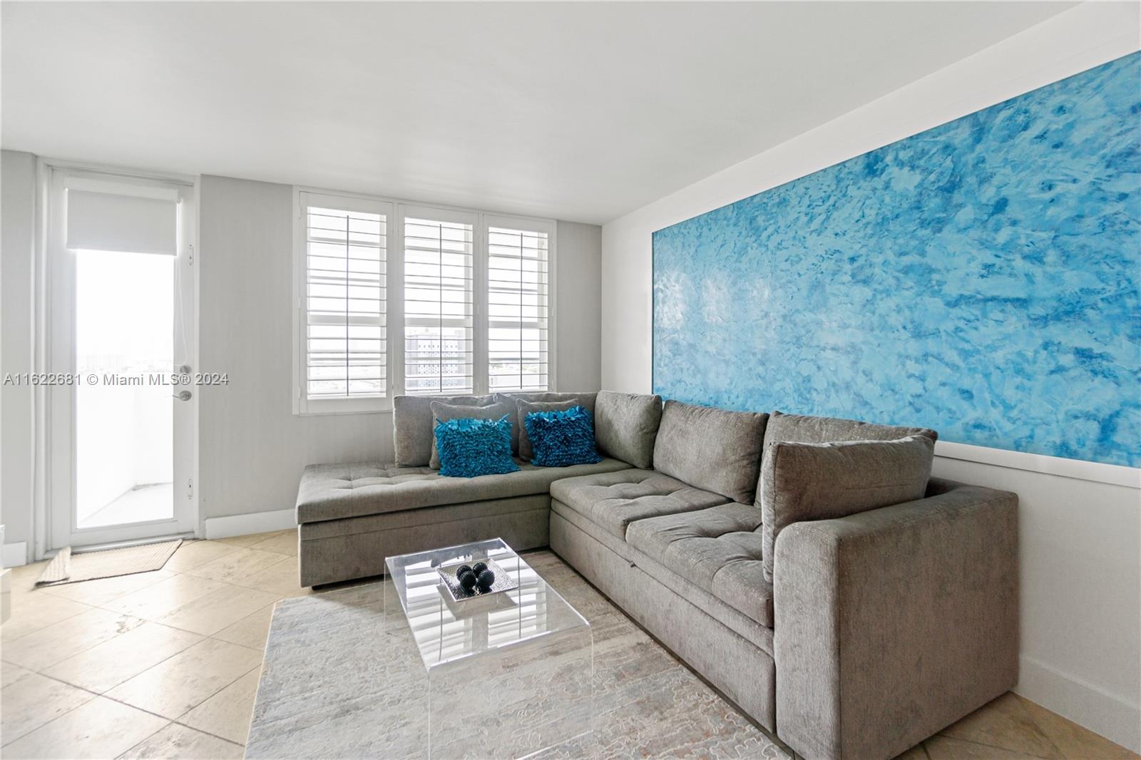 A living room features a grey sectional sofa, a glass coffee table, and a blue wall — 100 Lincoln Rd # 1422, Miami Beach FL 33139, MIAMI BEACH, FL