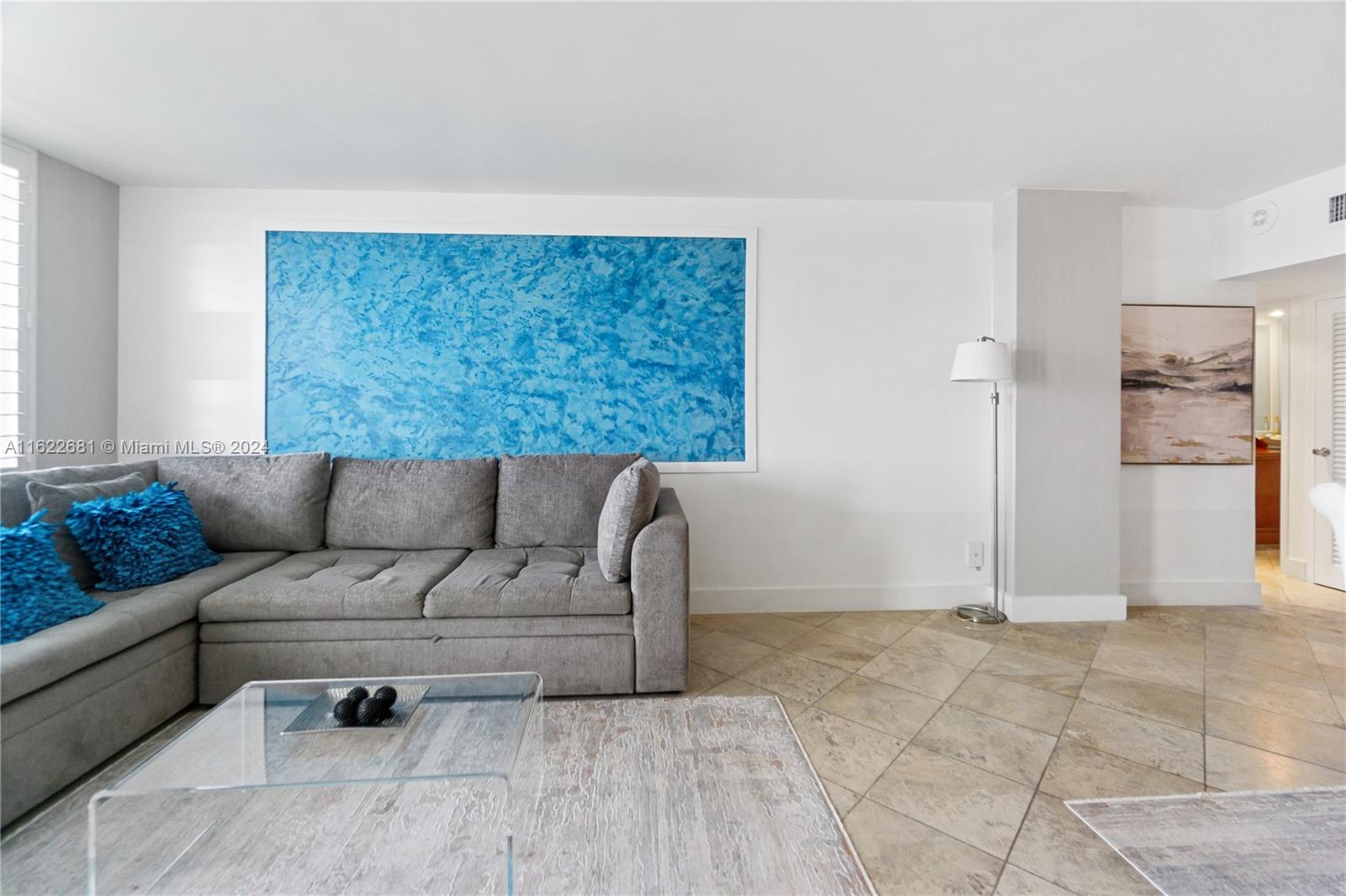 A living room features a gray sectional sofa, a blue textured wall panel, and tile flooring — 100 Lincoln Rd # 1422, Miami Beach FL 33139, MIAMI BEACH, FL