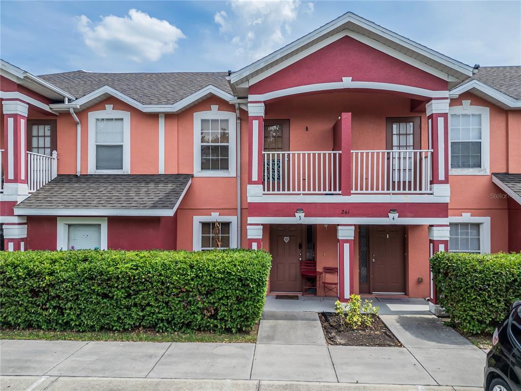 A two-story townhouse exterior features pink stucco walls, white trim, and a shared balcony — 261 AUTUMN LANE UNIT 3, KISSIMMEE, FL