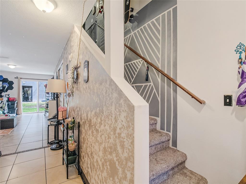 A staircase with a geometric painted wall mural sits beside a tiled living area — 261 AUTUMN LANE UNIT 3, KISSIMMEE, FL