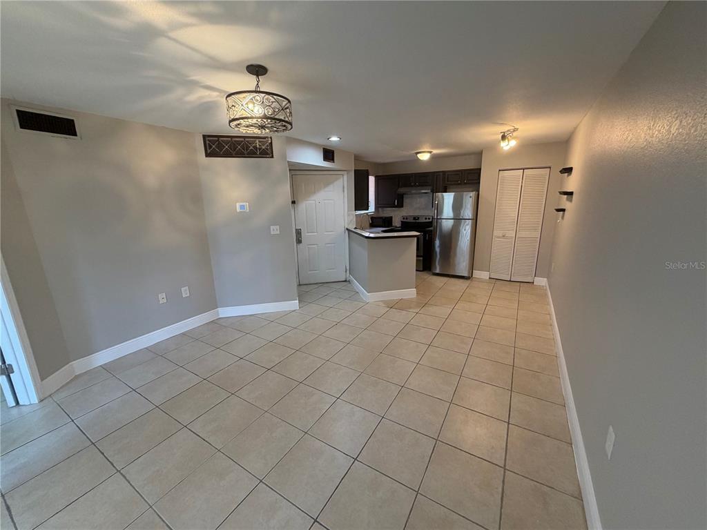 An open-concept living and kitchen area features light tile flooring and a decorative chandelier — 1916 LAKE ATRIUMS CIRCLE UNIT 28, ORLANDO, FL
