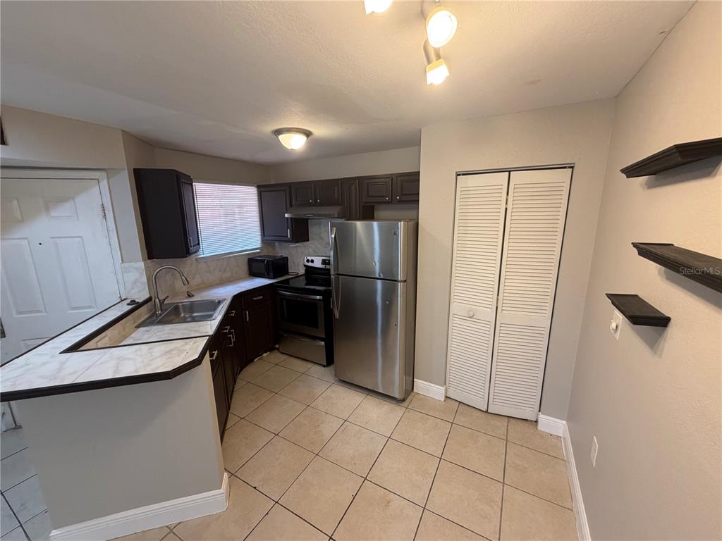 A kitchen features dark cabinets, stainless steel appliances, tile flooring, and a breakfast bar — 1916 LAKE ATRIUMS CIRCLE UNIT 28, ORLANDO, FL