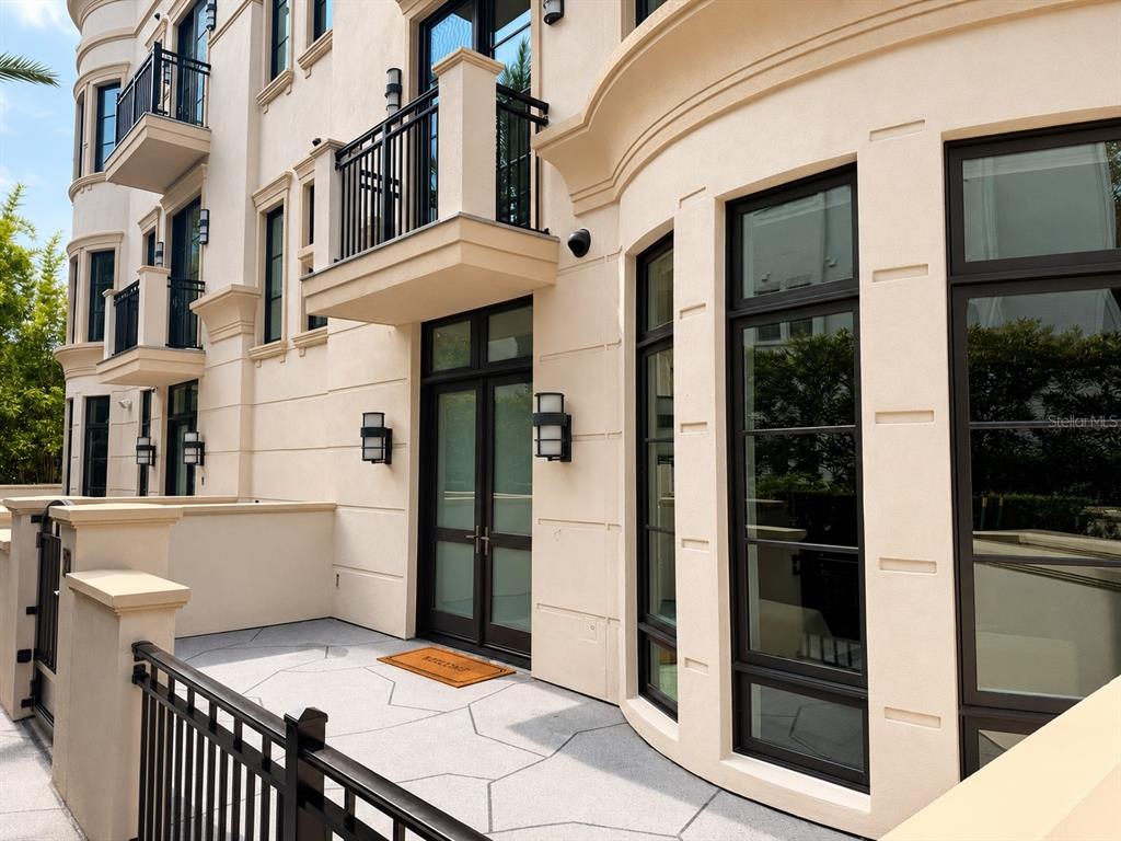 A beige building exterior features a ground-level patio, black-framed glass doors, and upper-level balconies — 125 S INTERLACHEN AVENUE UNIT 2, WINTER PARK, FL