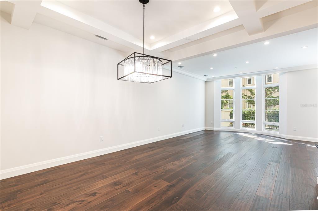 An empty room with dark hardwood floors, a coffered ceiling, and a modern crystal chandelier — 125 S INTERLACHEN AVENUE UNIT 2, WINTER PARK, FL