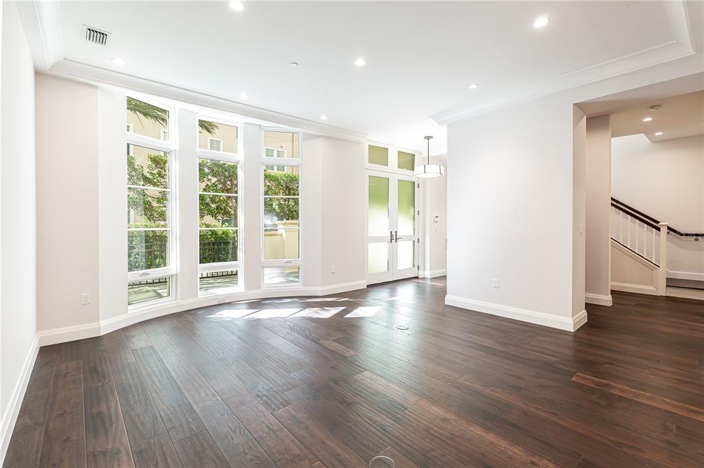 A bright room with dark wood floors, large windows, and a staircase in the background — 125 S INTERLACHEN AVENUE UNIT 2, WINTER PARK, FL