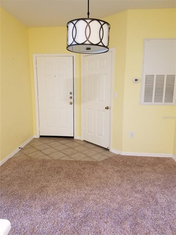An entryway features a tile floor, carpeted living area, yellow walls, and a drum pendant light — 5455 VINELAND ROAD UNIT 3303, ORLANDO, FL