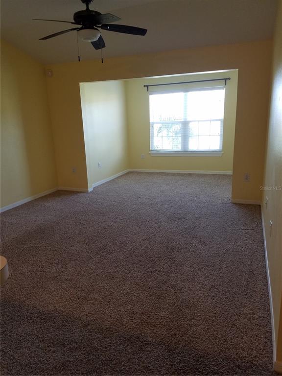 A carpeted room with yellow walls, a ceiling fan, and a recessed window area — 5455 VINELAND ROAD UNIT 3303, ORLANDO, FL