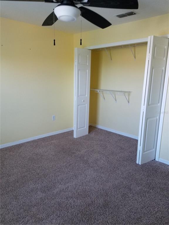 A bedroom with yellow walls, brown carpet, a ceiling fan, and an open white closet — 5455 VINELAND ROAD UNIT 3303, ORLANDO, FL