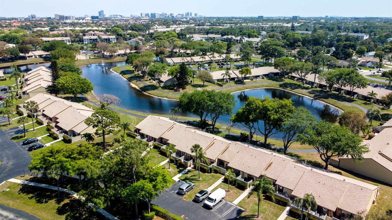 An aerial view shows residential townhouses arranged around a winding lake in a suburban setting — 1017 Green Pine Boulevard # C, West Palm Beach FL 33409, WEST PALM BEACH, FL