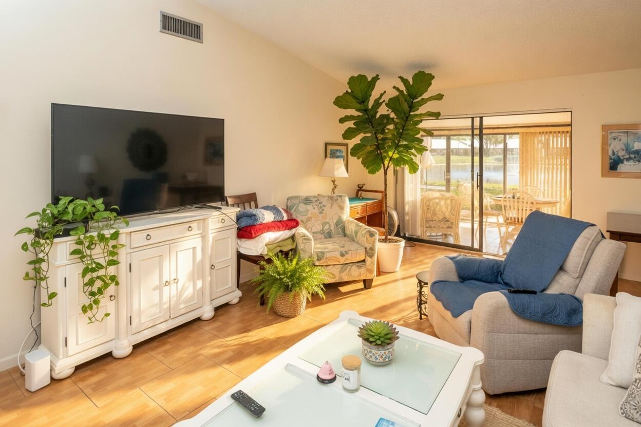 A living room with a white media console, patterned armchair, recliner, and a large potted plant — 1017 Green Pine Boulevard # C, West Palm Beach FL 33409, WEST PALM BEACH, FL