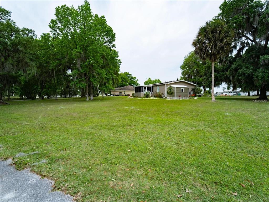 A grassy yard leads to a single-story house with a screened porch and large trees — LOT 30 BLK C OXFORD COURT, WILDWOOD, FL