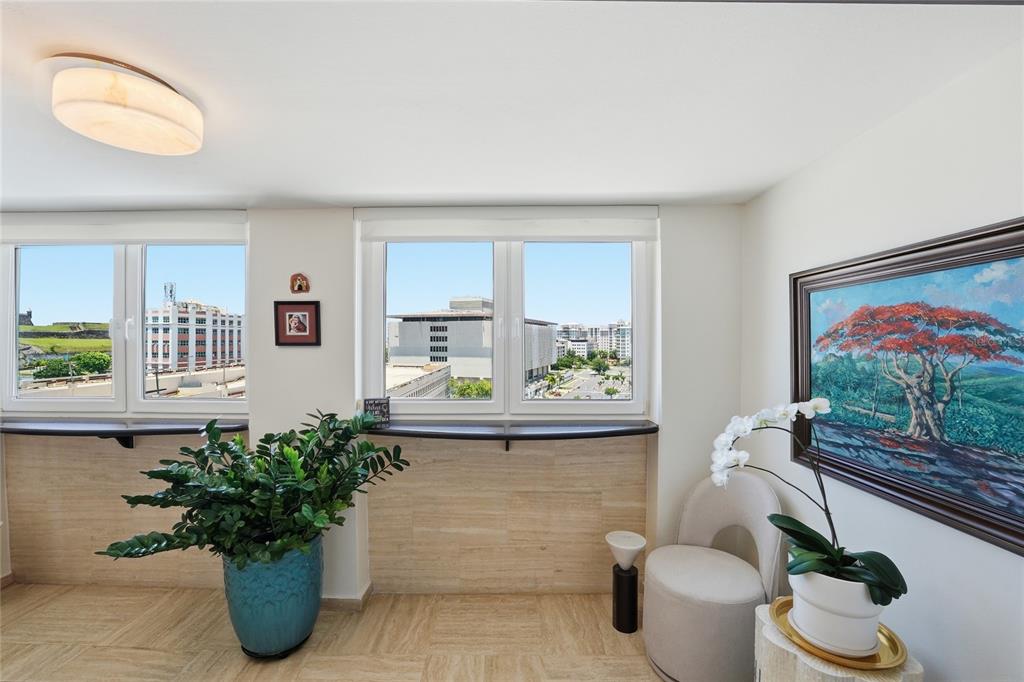 A room with travertine floors, two windows overlooking a city, a plant, and a chair — 100 JUAN A. CORRETJER UNIT PH-705, OLD SAN JUAN, PR