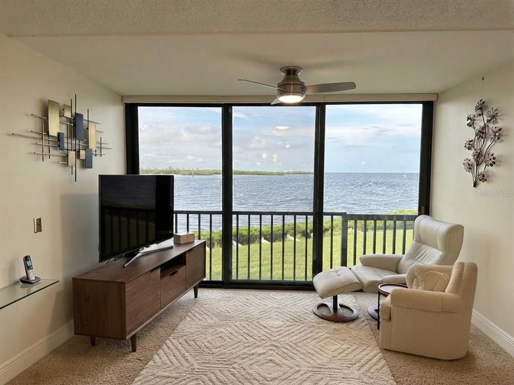 A living room features a television, a recliner with ottoman, and a large windowed water view — 4620 BAY BOULEVARD UNIT 1112, PORT RICHEY, FL