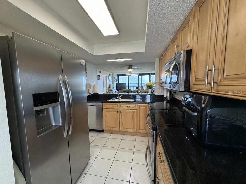 A kitchen features stainless steel appliances, light wood cabinets, and black countertops with tile flooring — 4620 BAY BOULEVARD UNIT 1112, PORT RICHEY, FL