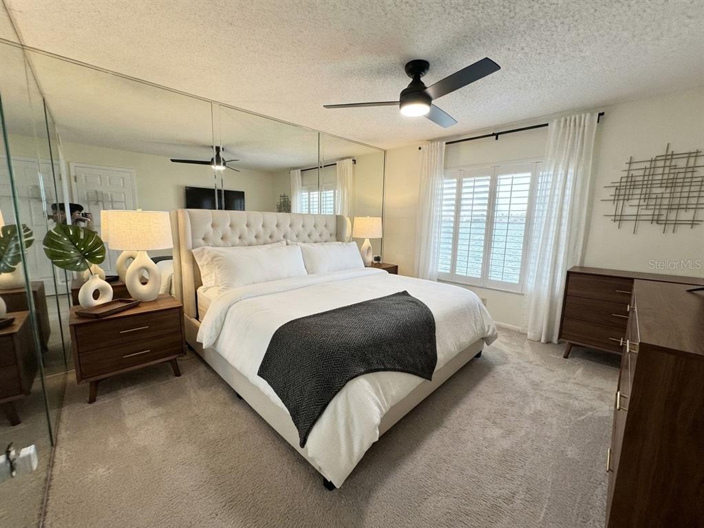 A bedroom features a tufted headboard, mirrored wall, ceiling fan, and dark wood furniture — 4620 BAY BOULEVARD UNIT 1112, PORT RICHEY, FL