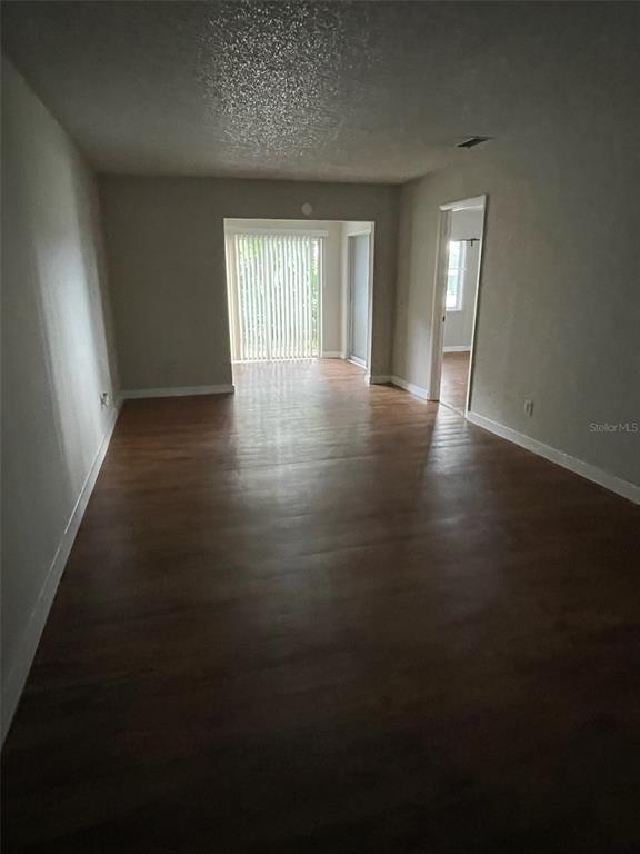 An empty living room features wood-look flooring, light-colored walls, and a sliding glass door — 2001 SAN MARCOS DRIVE SE UNIT 11, WINTER HAVEN, FL