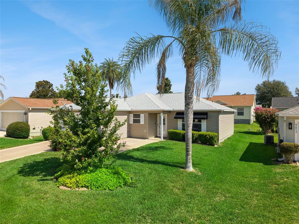 A single-story tan house with a palm tree in the front yard under a blue sky — 9603 SE 171ST ARGYLL STREET, THE VILLAGES, FL