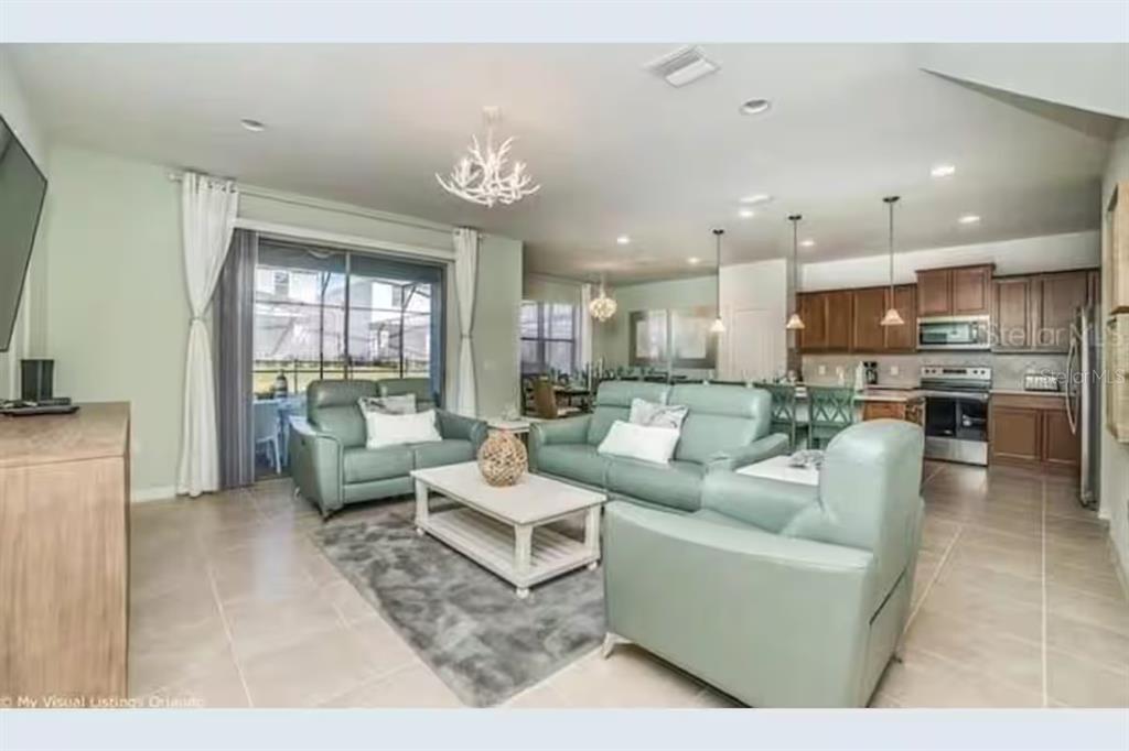 An open-concept living room and kitchen featuring light green furniture and tile flooring — 8933 PRAGUE WAY, KISSIMMEE, FL