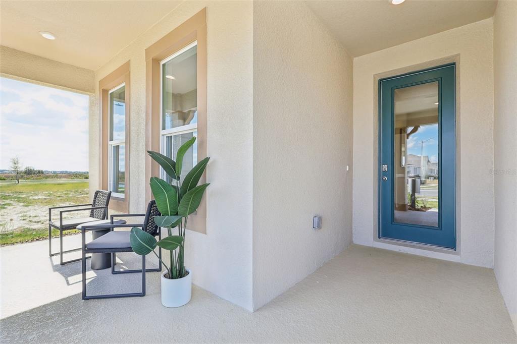 A covered porch features a blue glass-paneled door, two outdoor chairs, and a potted plant — 5308 CLOUDBERRY AVENUE, LAKELAND, FL