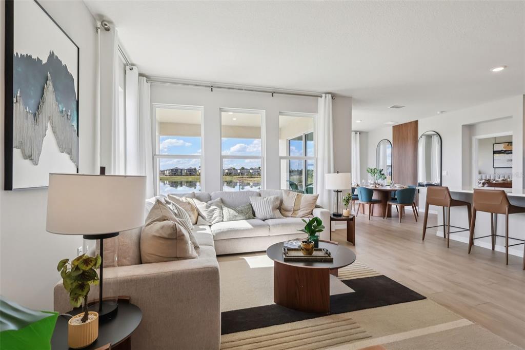 A bright living room features a sectional sofa, a coffee table, and large windows overlooking water — 5308 CLOUDBERRY AVENUE, LAKELAND, FL
