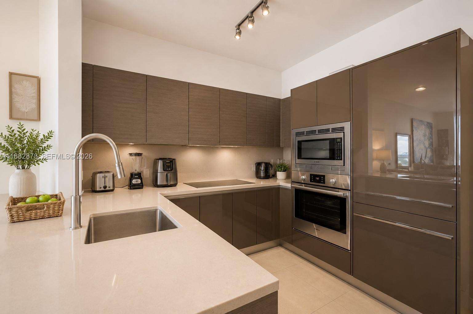 A modern kitchen features brown wood-grain upper cabinets, glossy taupe lower cabinets, and stainless steel appliances — 1080 Brickell Ave # 2503, Miami FL 33131, MIAMI, FL