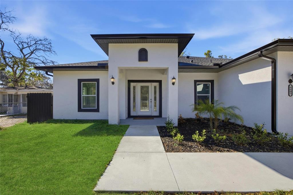A white single-story house with a black-trimmed front door, dark roof, and concrete walkway — 6605 24TH AVENUE S, TAMPA, FL