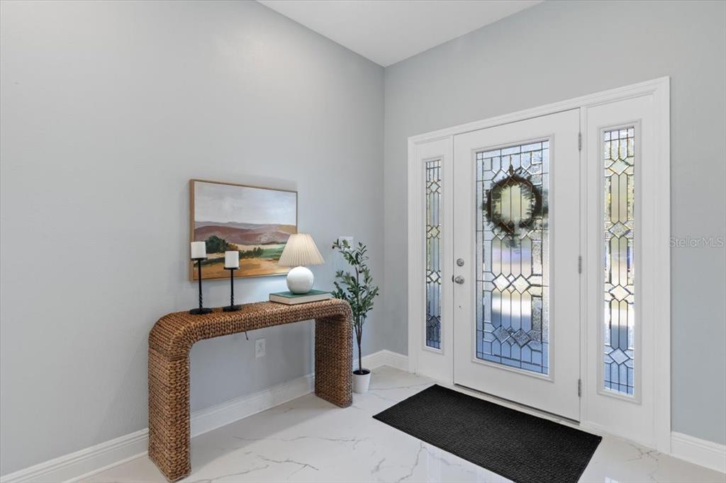 An entryway features a wicker console table, a lamp, artwork, and a white front door — 6605 24TH AVENUE S, TAMPA, FL