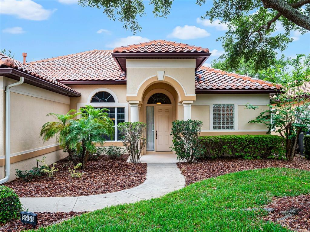A single-story house exterior features a tiled roof, arched entryway, and a landscaped front yard — 9958 SANTA BARBARA COURT, HOWEY IN THE HILLS, FL