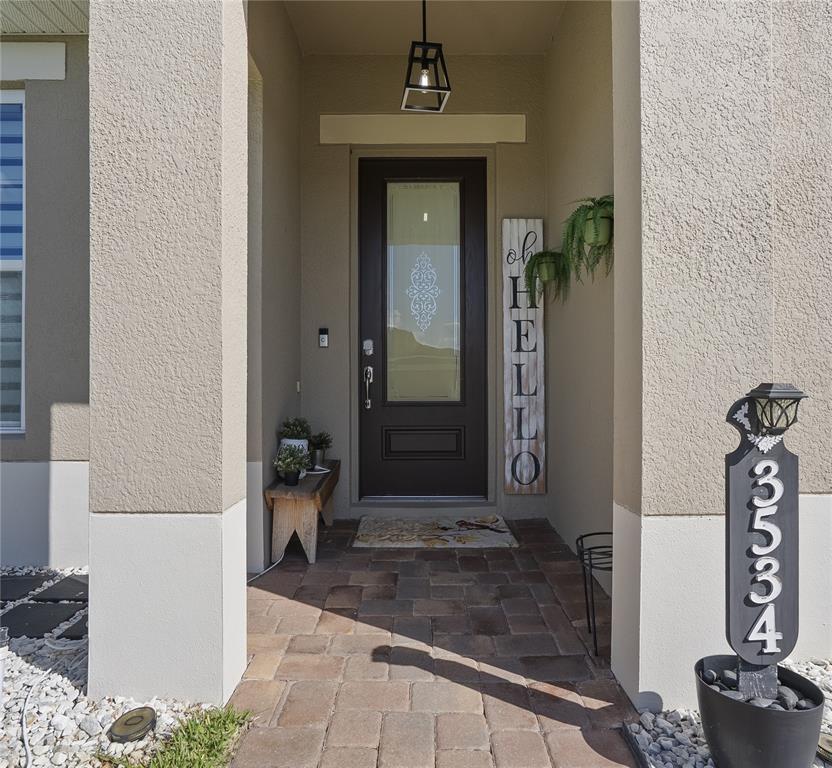 A covered entryway features a dark brown front door, a vertical hello sign, and pavers — 3534 CAYUGAS LOOP, ST CLOUD, FL