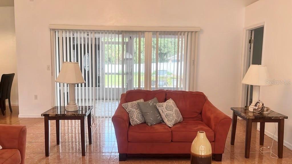 A living room features a red sofa, two end tables with lamps, and vertical window blinds — 619 MAYAN PLACE, KISSIMMEE, FL