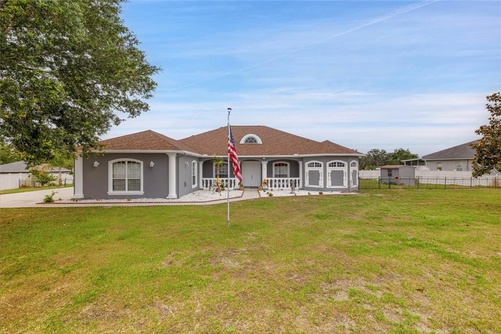 A single-story gray house with a brown roof, white trim, and an American flag — 5104 BIG STAND LANE, WIMAUMA, FL