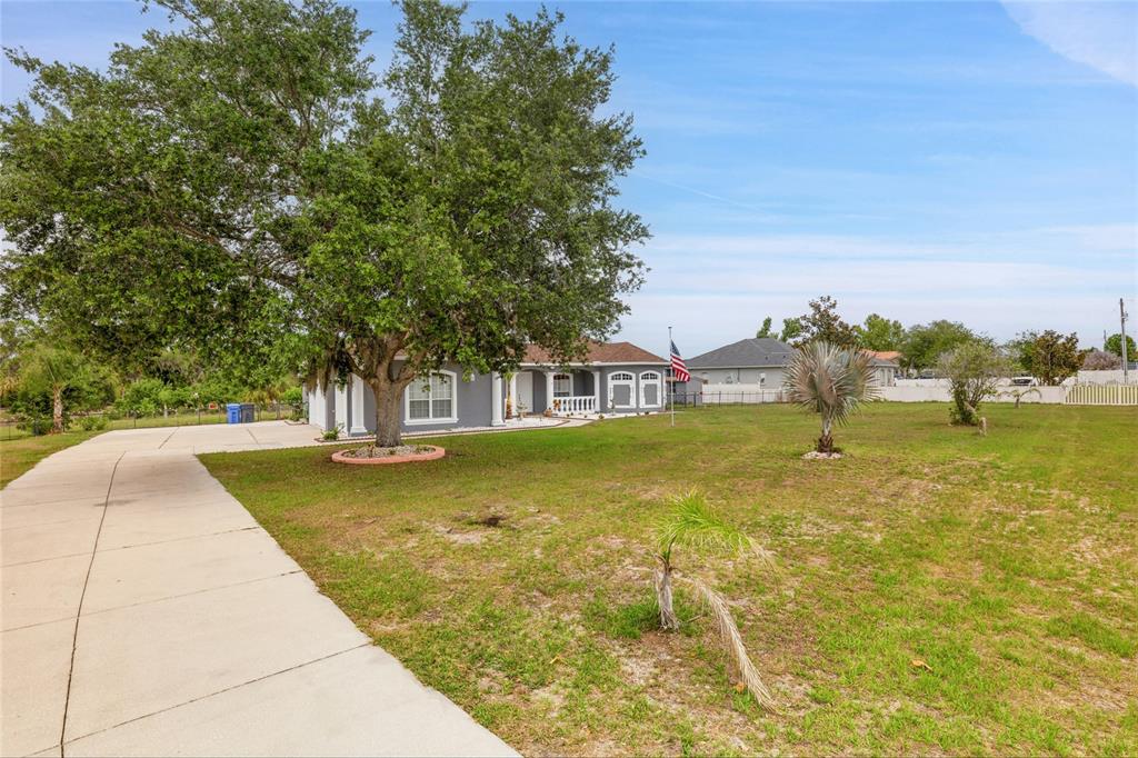 A gray house with a large tree and a concrete driveway sits on a lawn — 5104 BIG STAND LANE, WIMAUMA, FL