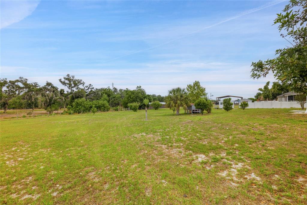 A large, grassy backyard features scattered trees, a small shed, and a white fence — 5104 BIG STAND LANE, WIMAUMA, FL