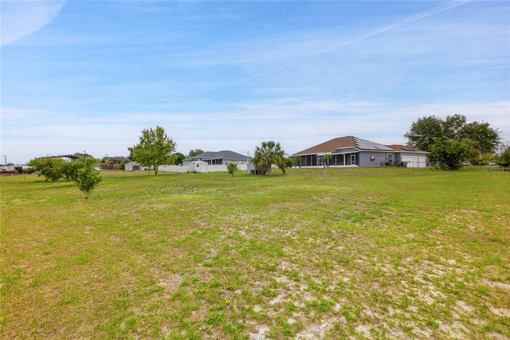 A large, grassy backyard features scattered trees and a view of neighboring houses — 5104 BIG STAND LANE, WIMAUMA, FL