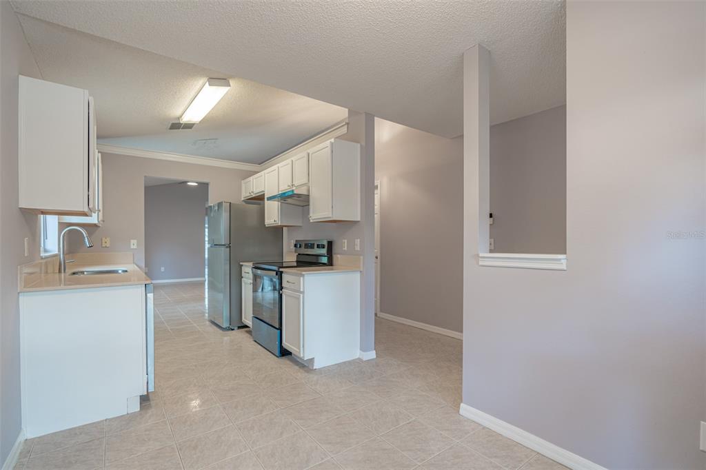 A kitchen features white cabinets, stainless steel appliances, and light-colored tile flooring — 5437 LEHIGH AVENUE, ORLANDO, FL