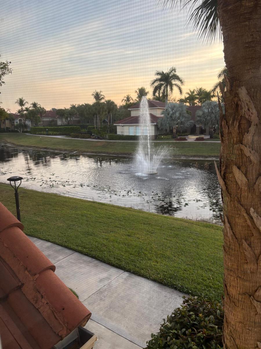 A view of a pond with a fountain, palm trees, and a building at sunset — 15075 Michelangelo Boulevard # 204, Delray Beach FL 33446, DELRAY BEACH, FL